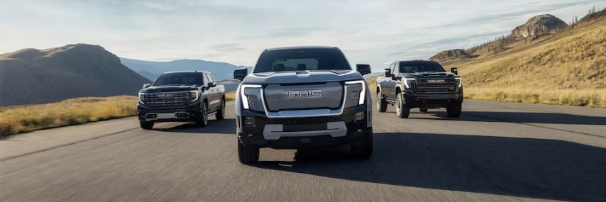 Three GMC Sierra trucks driving side by side on a mountain road with open terrain in the background.